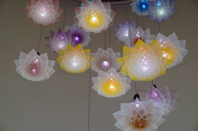 Een stuk of 15 robot bloemen die kunnen bewegen hangen van een plafond met verschillende kleuren licht.