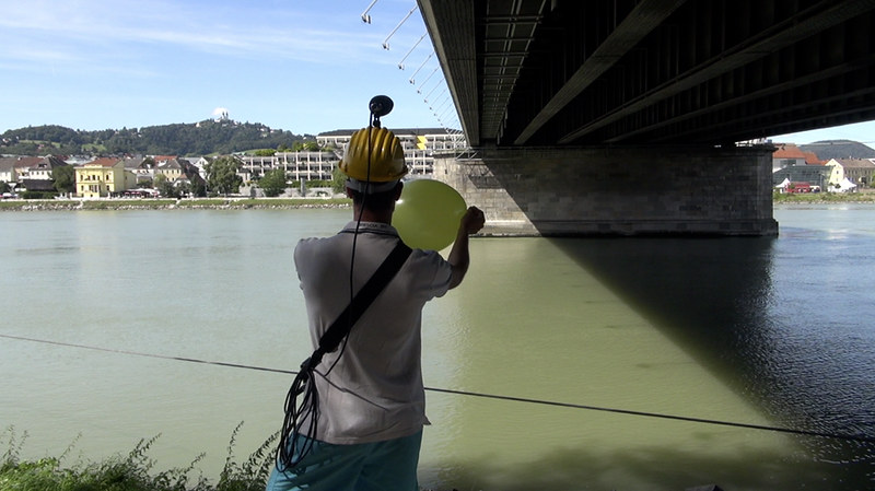Een kunstenaar uit Davide Tidoni's project 'A Balloon for' onderzoekt akoestiek in verschillende ruimtes door een ballon te knappen onder een brug en dit geluid op te nemen.