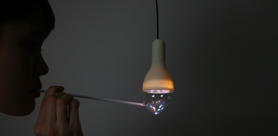 Zijaanzicht van een persoon die een bel blaast in een rietje met bellenblaas, waardoor een bel tegen een lamp aankomt en aangaat,