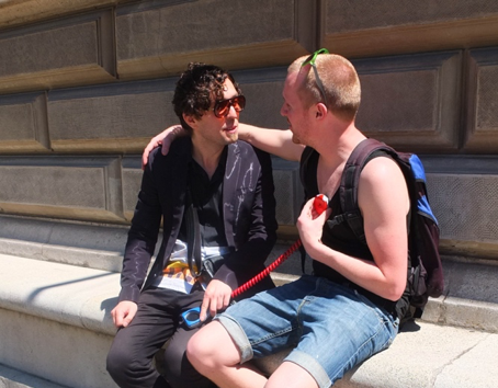 Twee mannen zitten op een stoep en gebruiken een apparaat waarmee je elkaar een ritme kan sturen als vorm van communicatie.