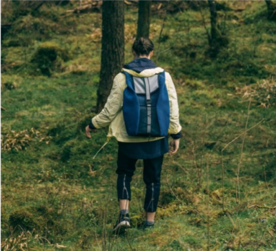 Een persoon loopt naar beneden over gras, draagt wandelkleding en een bijzondere rugzak die energie kan opwekken doordat het gemaakt is met heel kleine zonnepanelen.