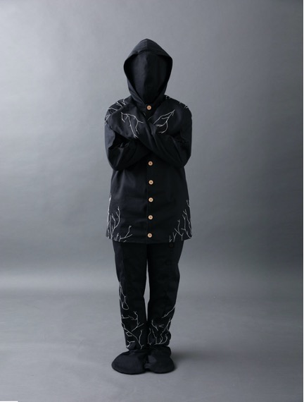 Model draagt Burial Suit, in zwart, dat met schimmels het lichaam na de dood afbreekt en afvalstoffen verwerkt en zo duurzaam begraven mogelijk maakt.
